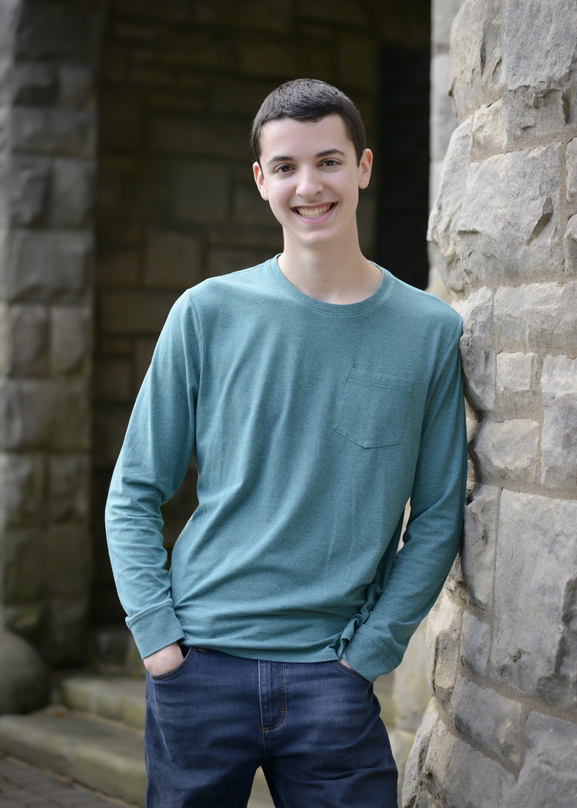 A portrait photograph of a man leaning against a stone wall